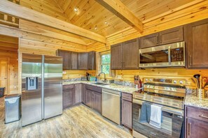 A modern kitchen with stainless steel appliances, wooden cabinetry, and a granite countertop. - The Havana Cabana | Log Cabin Escape (Bethlehem)