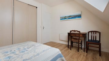 A bedroom with a bed, a desk, two chairs, a painting on the wall, and a sloped ceiling.