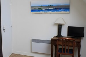 A room with a desk, a chair, a television, a lamp, a radiator, and a painting on the wall.