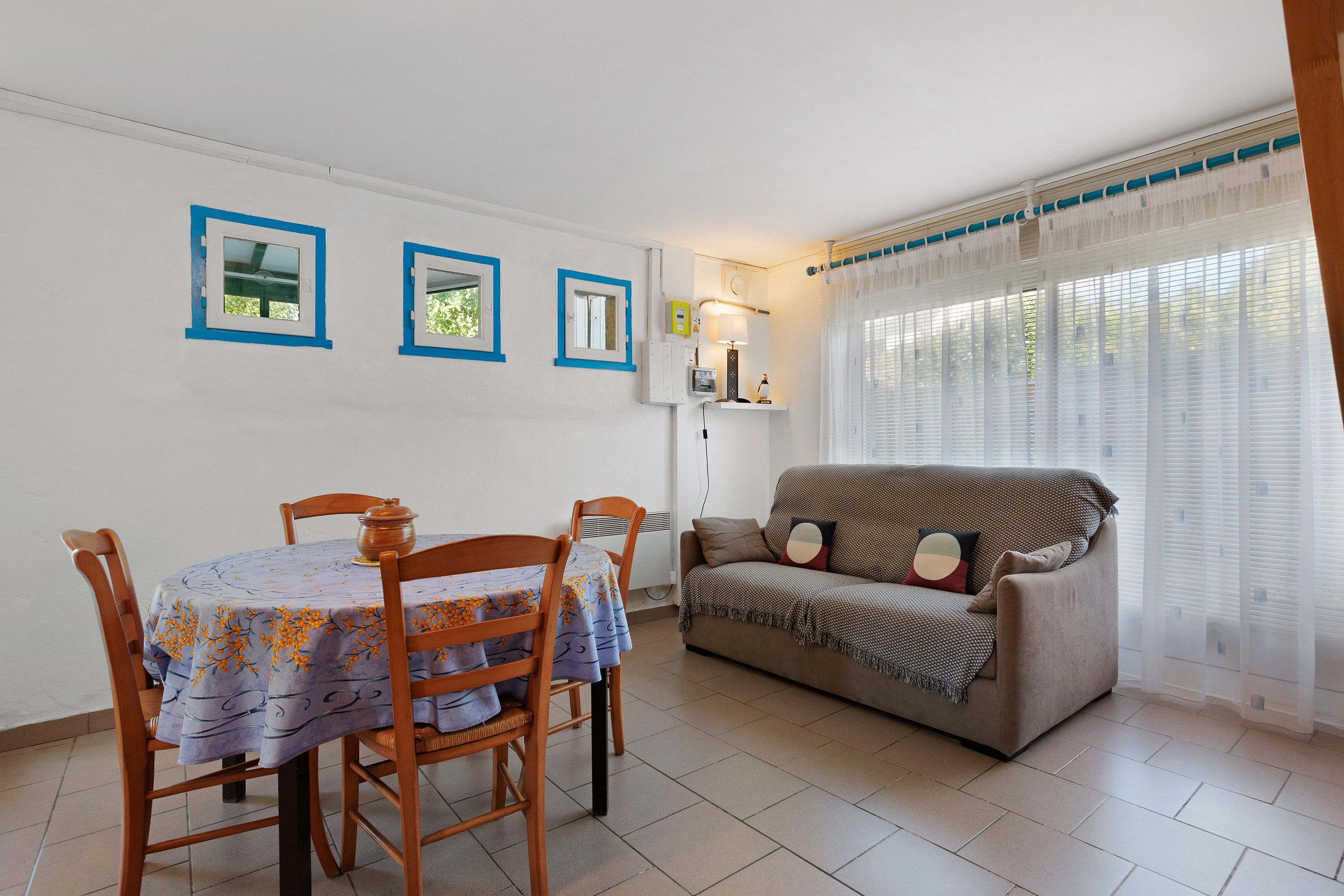 A dining area with a table and chairs, a sofa, and a window with curtains.