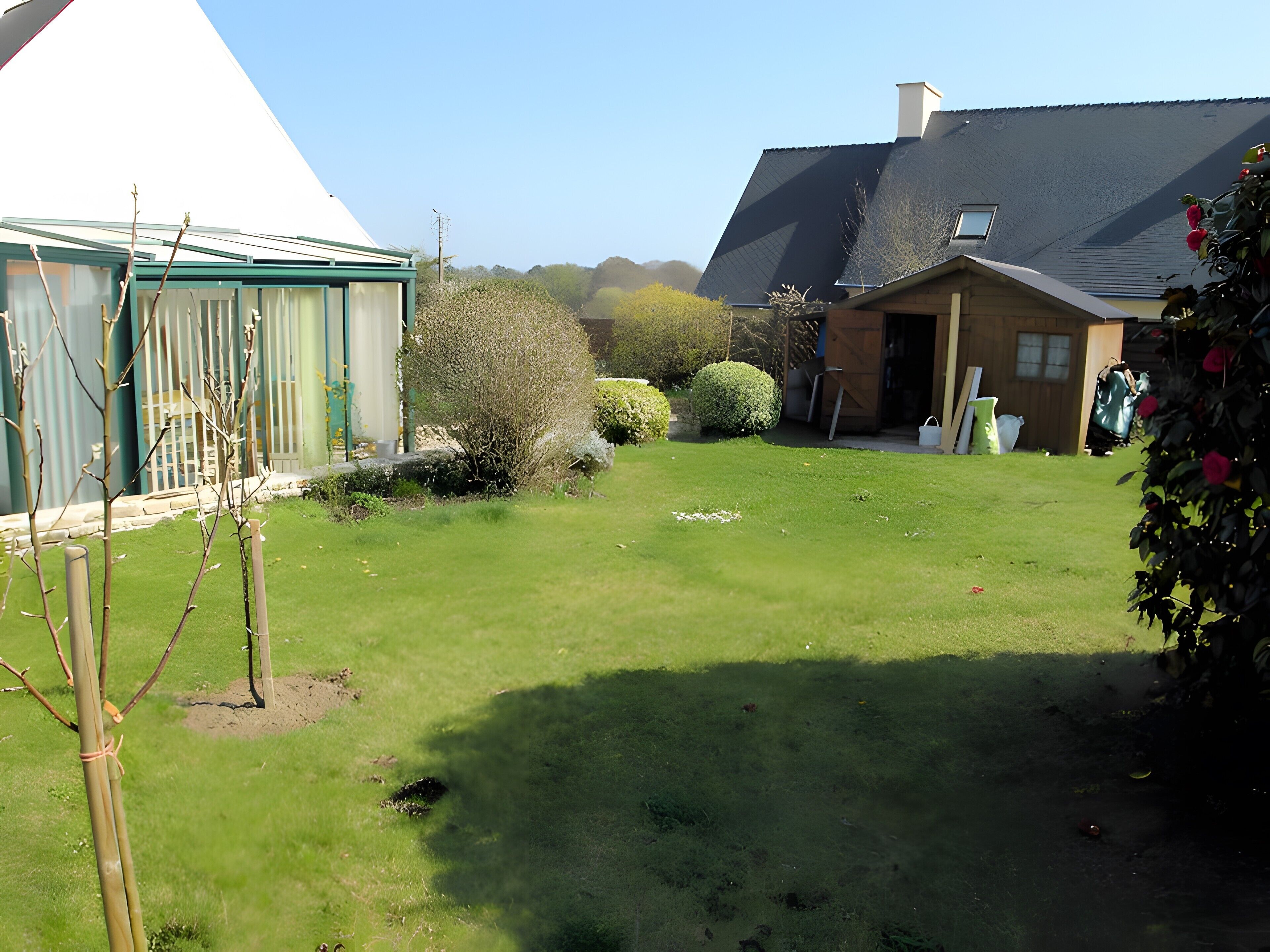 A well-maintained garden with a white gazebo, a wooden house, and a large tree.