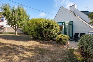 Il s'agit d'une propriété résidentielle comprenant une maison blanche, un espace extérieur aménagé avec un coin salon couvert et un jardin bien entretenu.