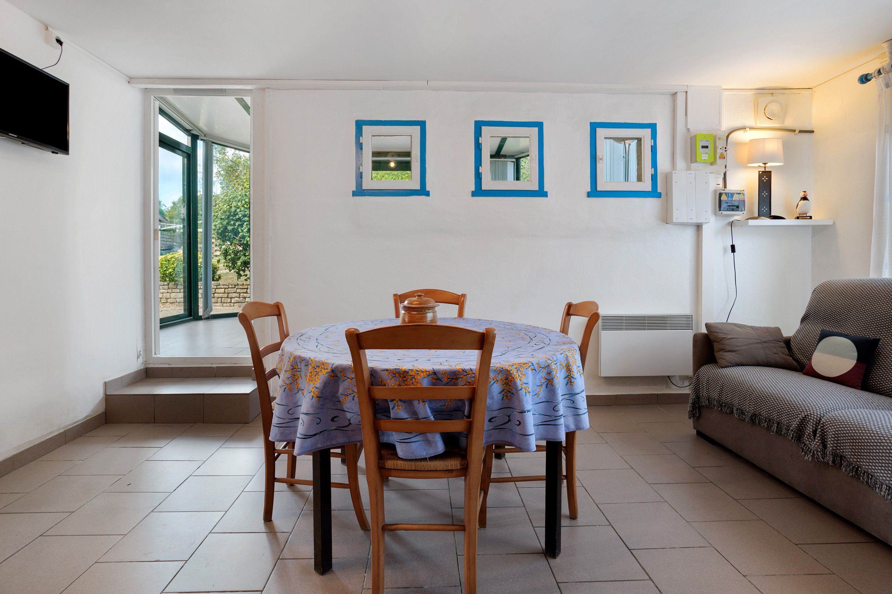 A dining area with a table and chairs, a sofa, and a window with a view of greenery.