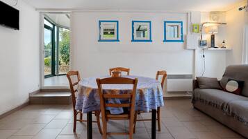 A dining area with a table and chairs, a sofa, and a window with a view of greenery.
