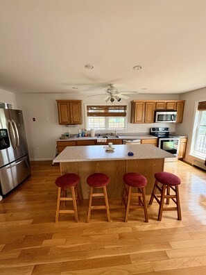 A kitchen with wooden cabinets, a stainless steel refrigerator, a microwave, and a stove. There are three red stools at the island. - 2 blocks to Roger Wheeler Beach 4-bedroom house perfect for your Summer getaway! (Narragansett)