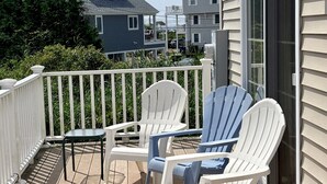 En træterrasse med to hvide Adirondack-stole og et lille bord, med udsigt over et boligområde.