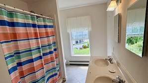 Et badeværelse med badeforhæng, et vindue, en vask og et spejl.