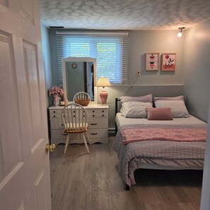 A bedroom with a bed, bedside table, lamp, chair, dresser, and a window with blinds. - Zen Cove- Home in West Saint John. 7 minutes from the Irving Nature Park. (Saint John)
