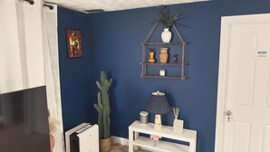 A room with a blue wall, a white door, a white console table with a lamp, a cactus, and a shelf with decorative items. - Zen Cove- Home in West Saint John. 7 minutes from the Irving Nature Park. (Saint John)