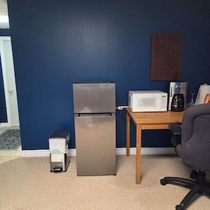 A room with a refrigerator, microwave, coffee maker, and a small trash bin.