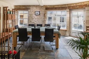 A dining area with a stone wall, large windows, and a wooden table set for six. - Tranquility House (Painswick)