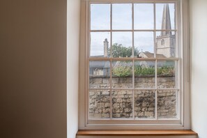 A window with a view of a stone wall and a church spire. - Tranquility House (Painswick)