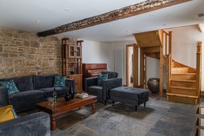 A living room with a stone wall, a wooden staircase, and a piano. - Finest Retreats | Tranquility House (Painswick)