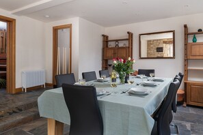 A dining room with a long table set for six, surrounded by chairs, with a vase of flowers and wine glasses on the table. - Tranquility House (Painswick)