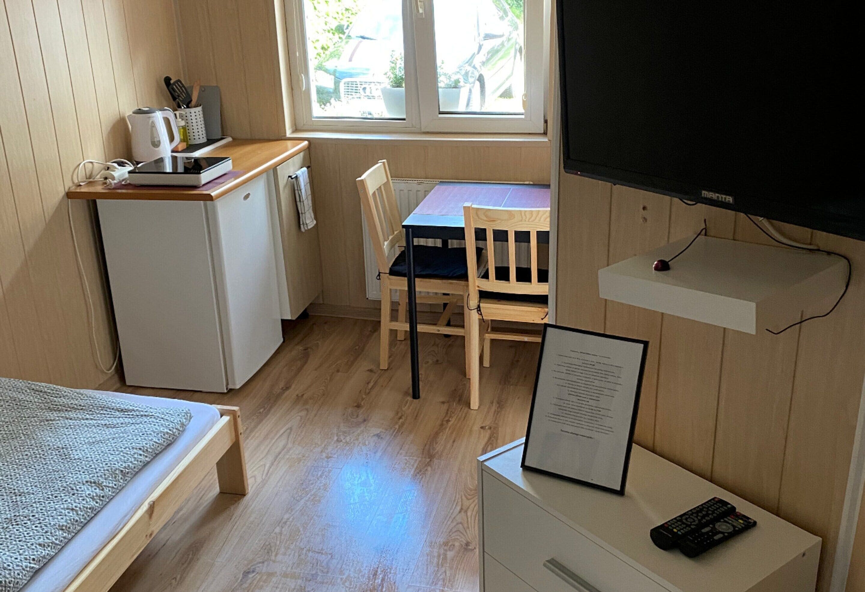 A compact room with a kitchenette, a dining table with chairs, a bed, and a TV.