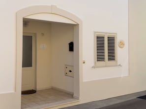 Un edificio blanco con una puerta, una ventana con contraventanas y un buzón pequeño.