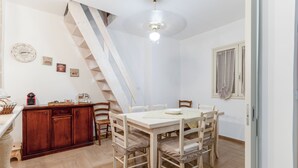 Un espace repas avec une table et des chaises en bois, un escalier et un coin cuisine équipé de placards et d’une machine à café.