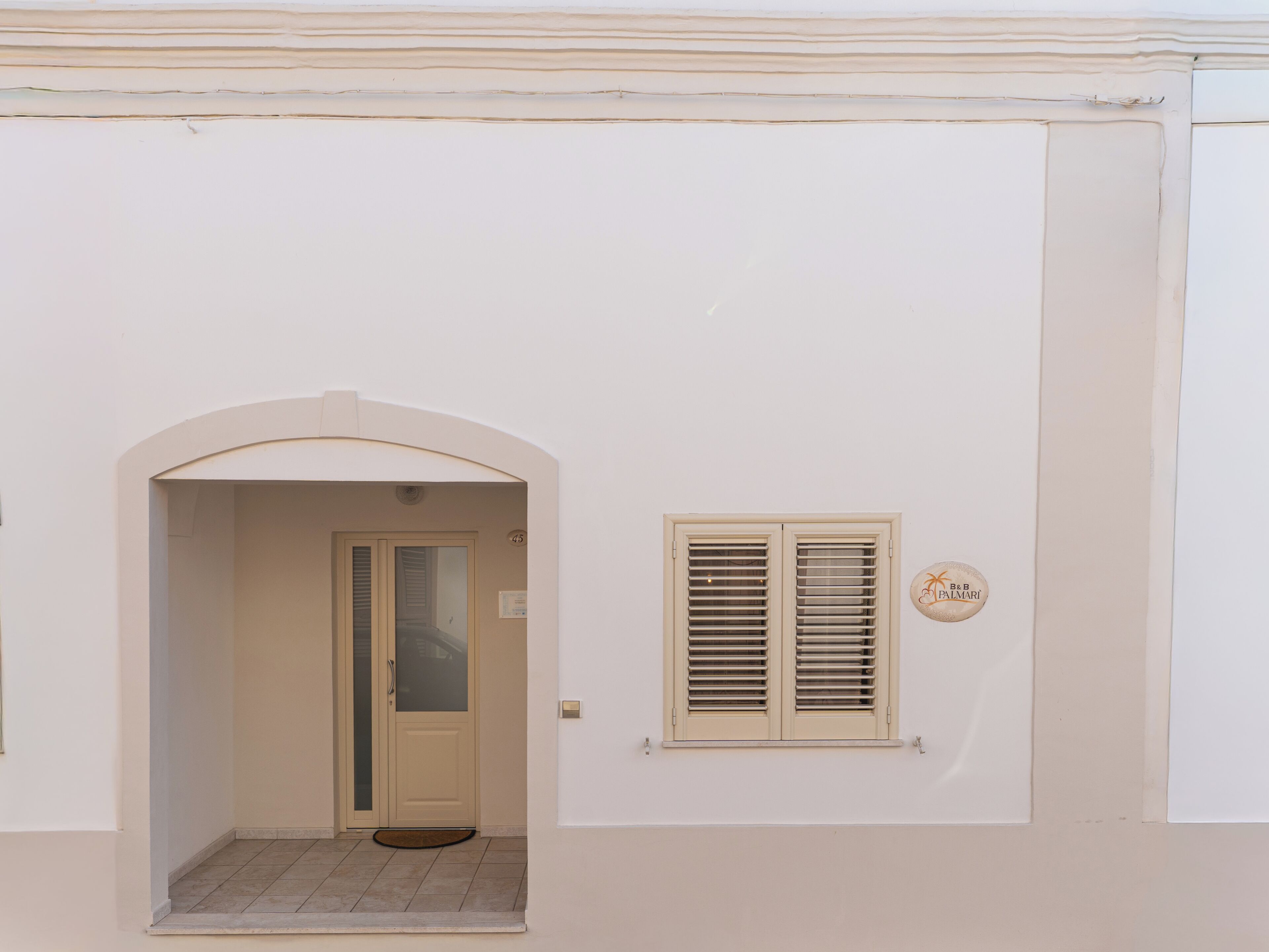 A building entrance with a door, a small window with shutters, and a doorbell.