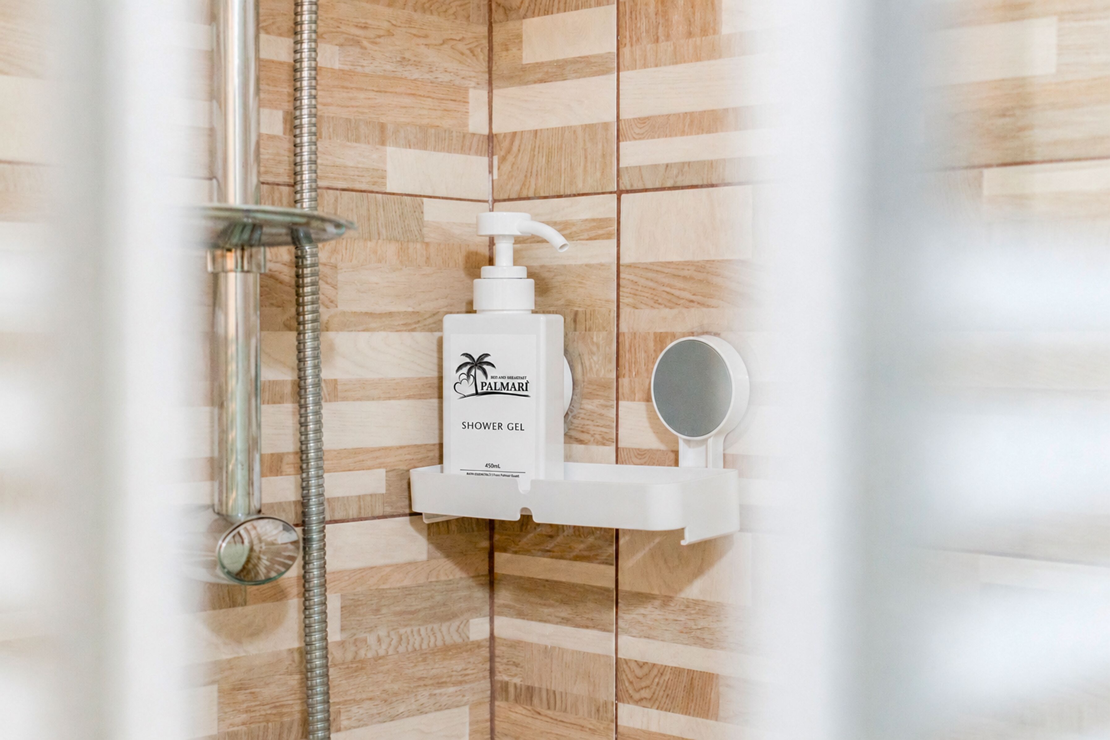 Un área de ducha con pared de madera, un cabezal de ducha manual, una botella de gel de ducha y un espejo de mano.