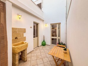 Een kleine binnenplaats met een stenen wasbak, een houten tafel en een deur naar een binnenruimte.