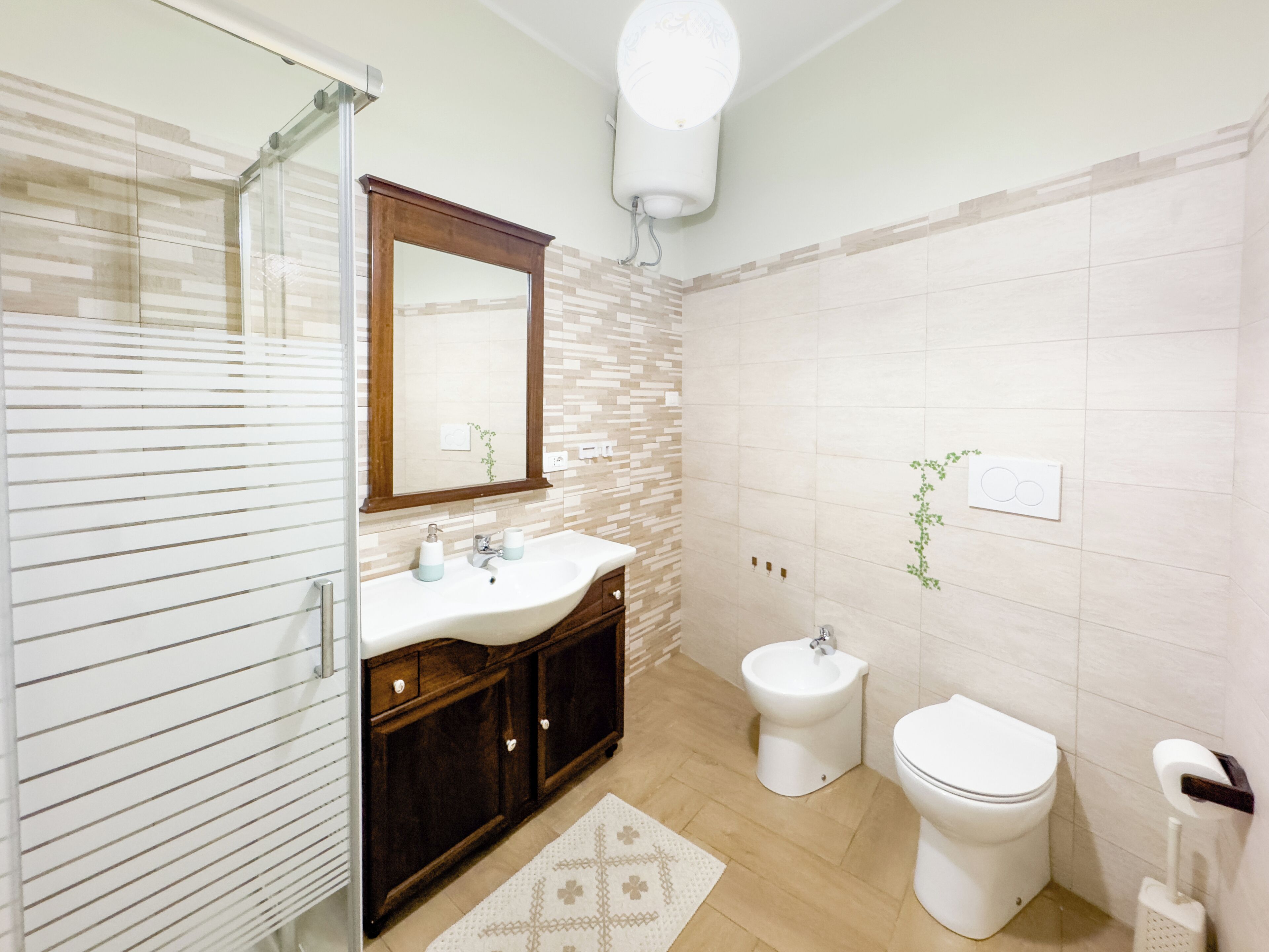 Un baño con cabina de ducha de vidrio, lavabo con espejo, bidé y retrete.