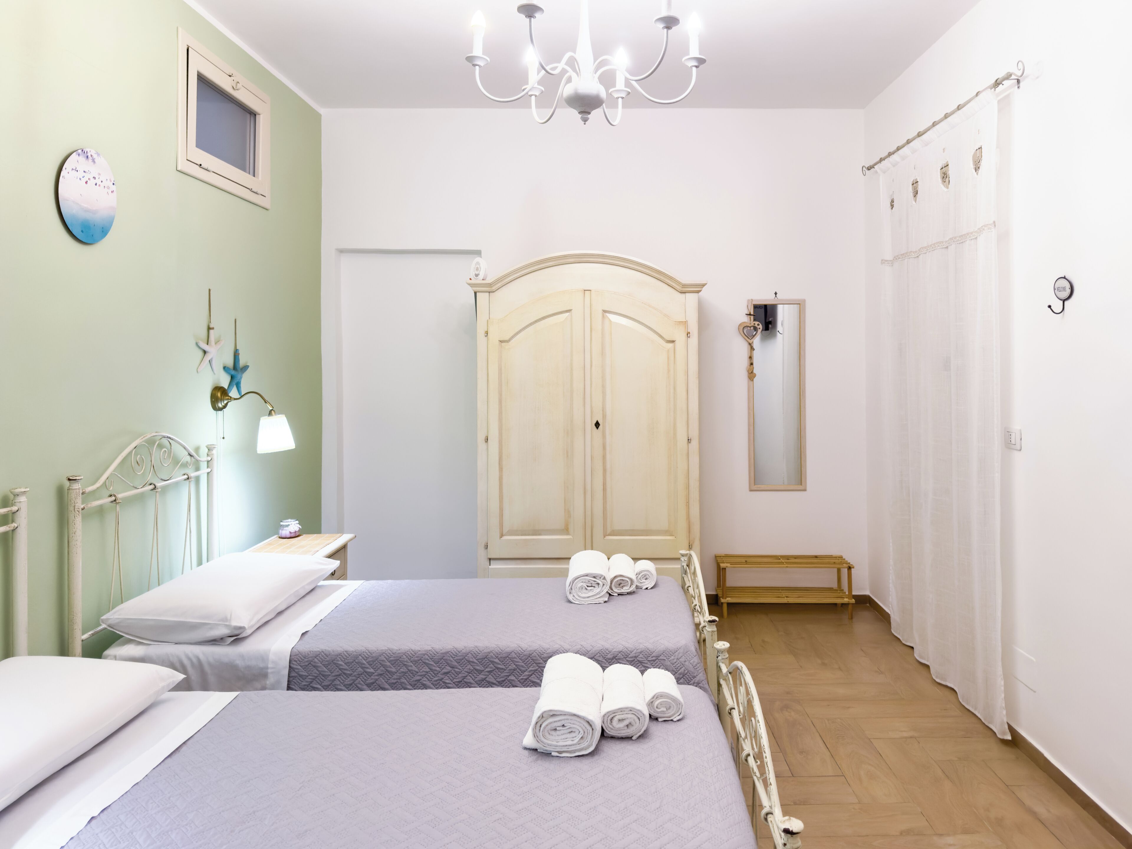 Une chambre d’hôtel avec deux lits, un lustre, une armoire et un miroir.