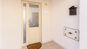 Une porte avec un panneau en verre, un paillasson, une boîte aux lettres fixée au mur et un interrupteur.