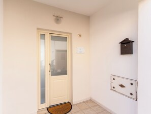 Una puerta con un panel de vidrio, un felpudo, un buzón en la pared y un interruptor de luz.