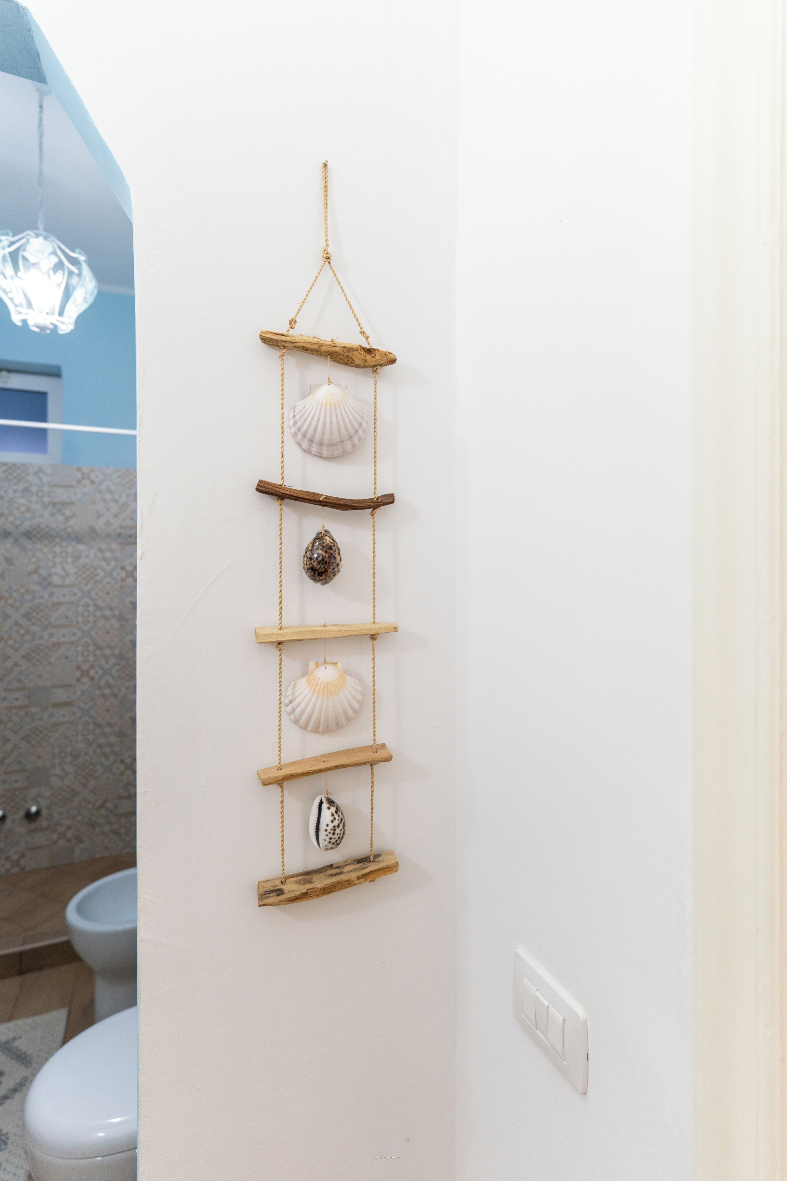 Eine an der Wand befestigte Holzablage mit Muscheln und einer Pendelleuchte.
