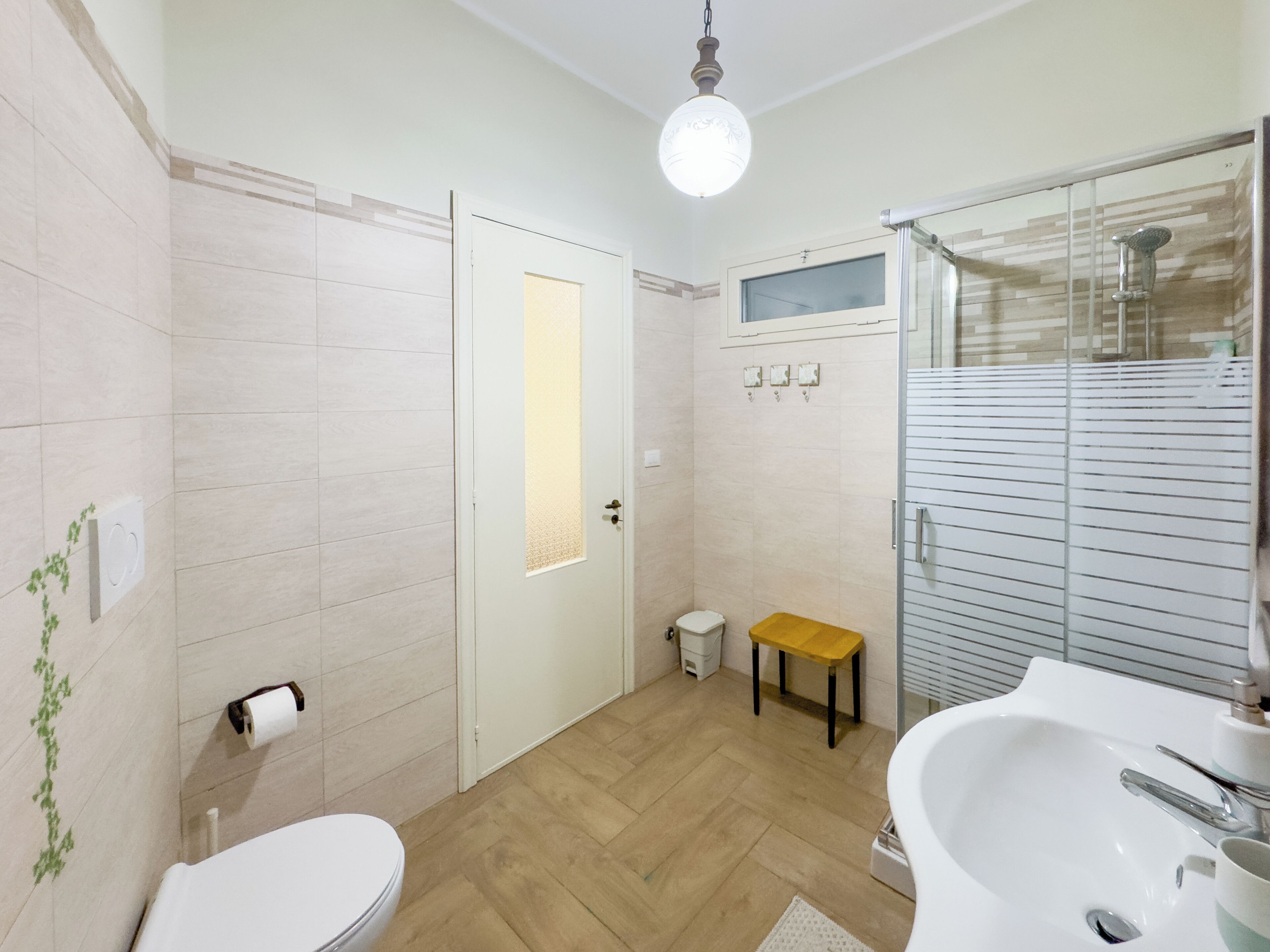 A bathroom with a toilet, a bench, a shower, and a sink.