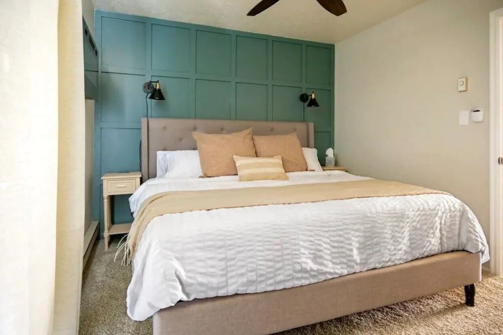 Een slaapkamer met een bed, nachtkastjes, een plafondventilator en een wand in turquoise kleur.