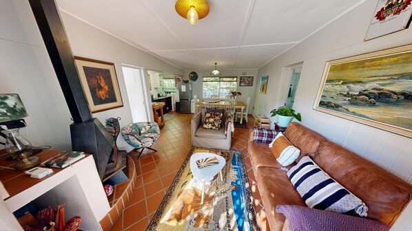 A living room with a sofa, armchair, and a coffee table. There is a painting on the wall and a plant on the floor.