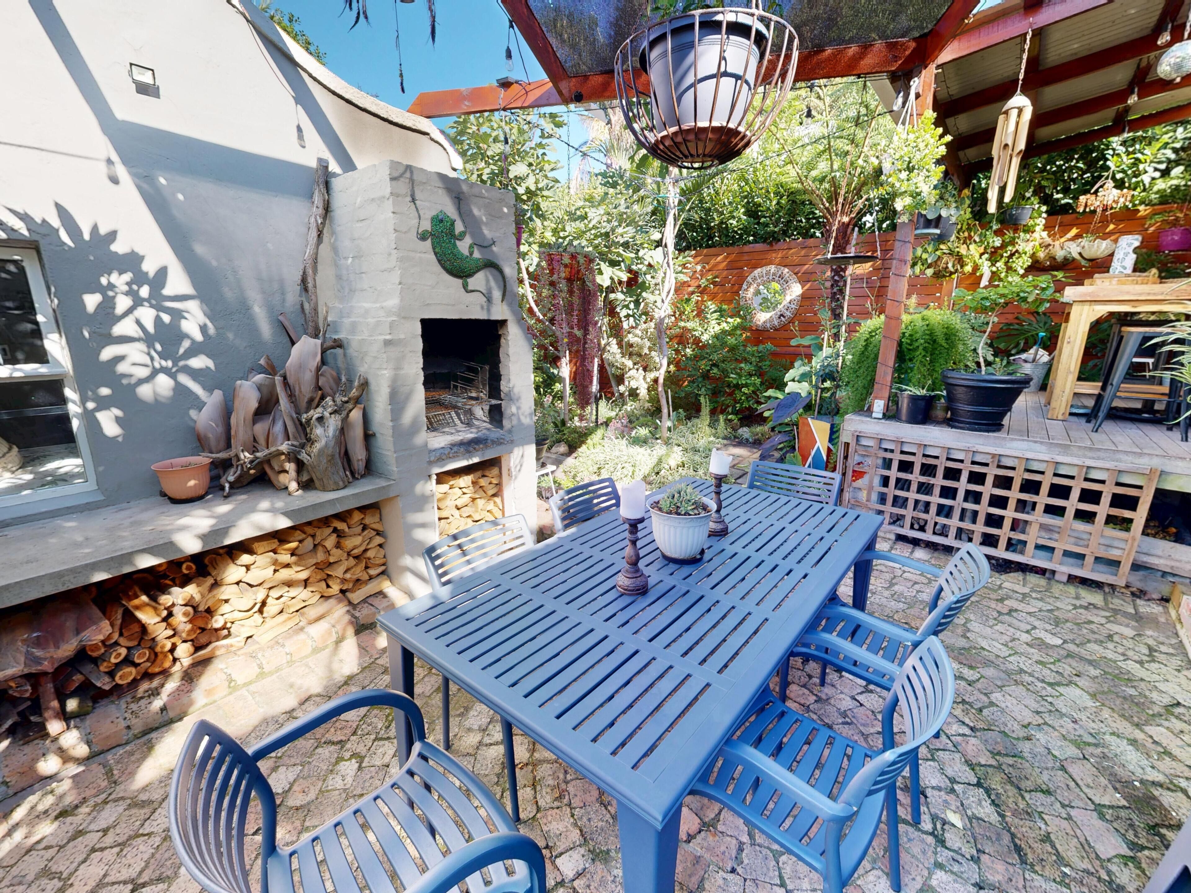 Un espace patio avec une table et des chaises, un mur en pierre avec une cheminée et diverses plantes en pot.