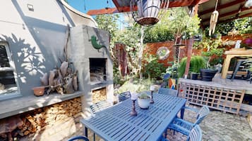 Un espace patio avec une table et des chaises, un mur en pierre avec une cheminée et diverses plantes en pot.