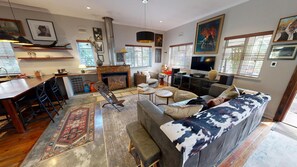 A spacious living area with a sofa, coffee table, and a fireplace. There is a television and a dining area with a bar.