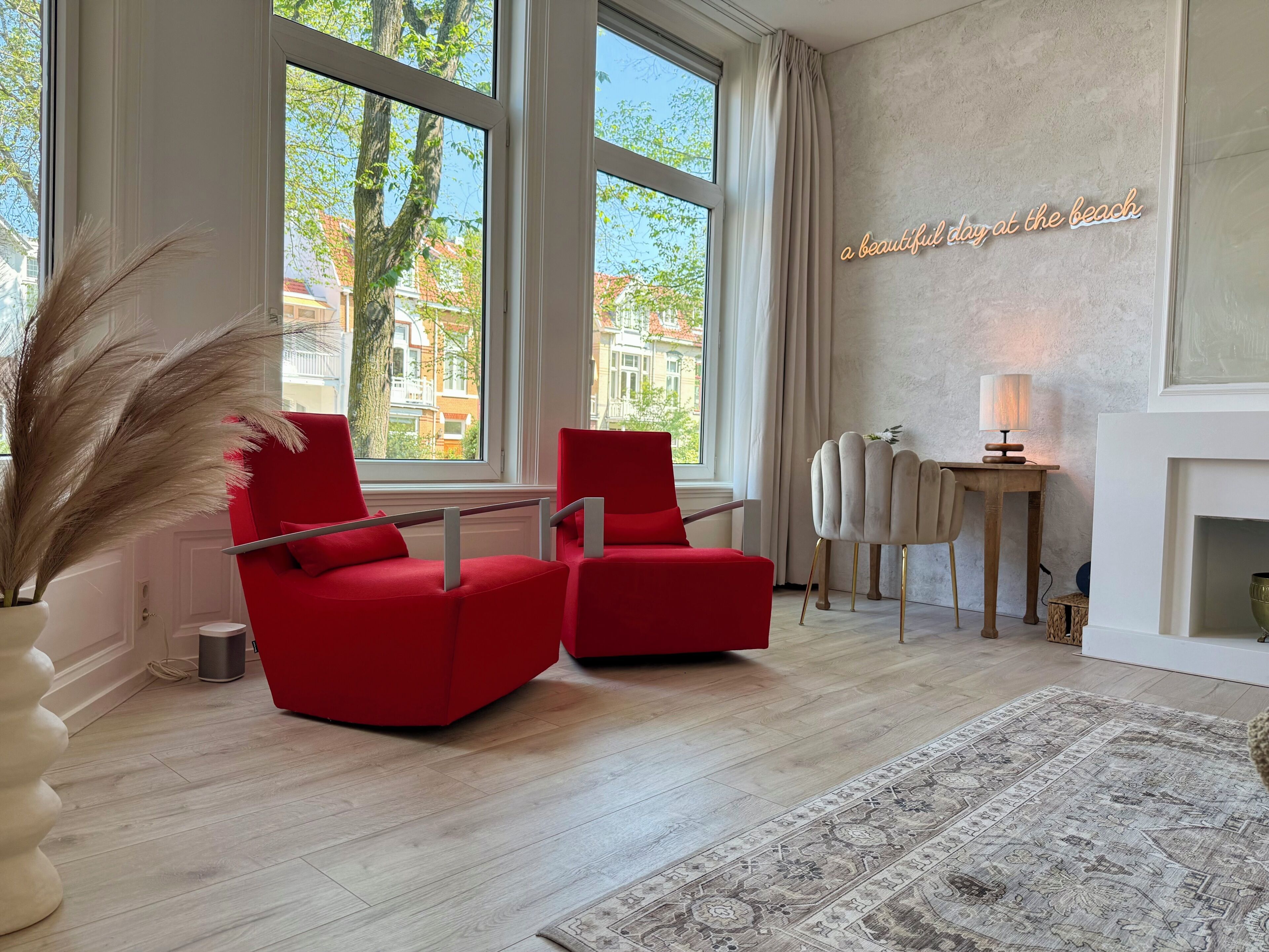 Een moderne woonkamer met grote ramen, een rode bank, een bijzettafeltje en een decoratieve lamp.
