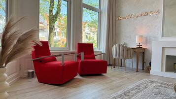 Een moderne woonkamer met grote ramen, een rode bank, een bijzettafeltje en een decoratieve lamp.