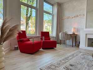 Ein modernes Wohnzimmer mit großen Fenstern, einem roten Sofa, einem Beistelltisch und einer dekorativen Lampe.