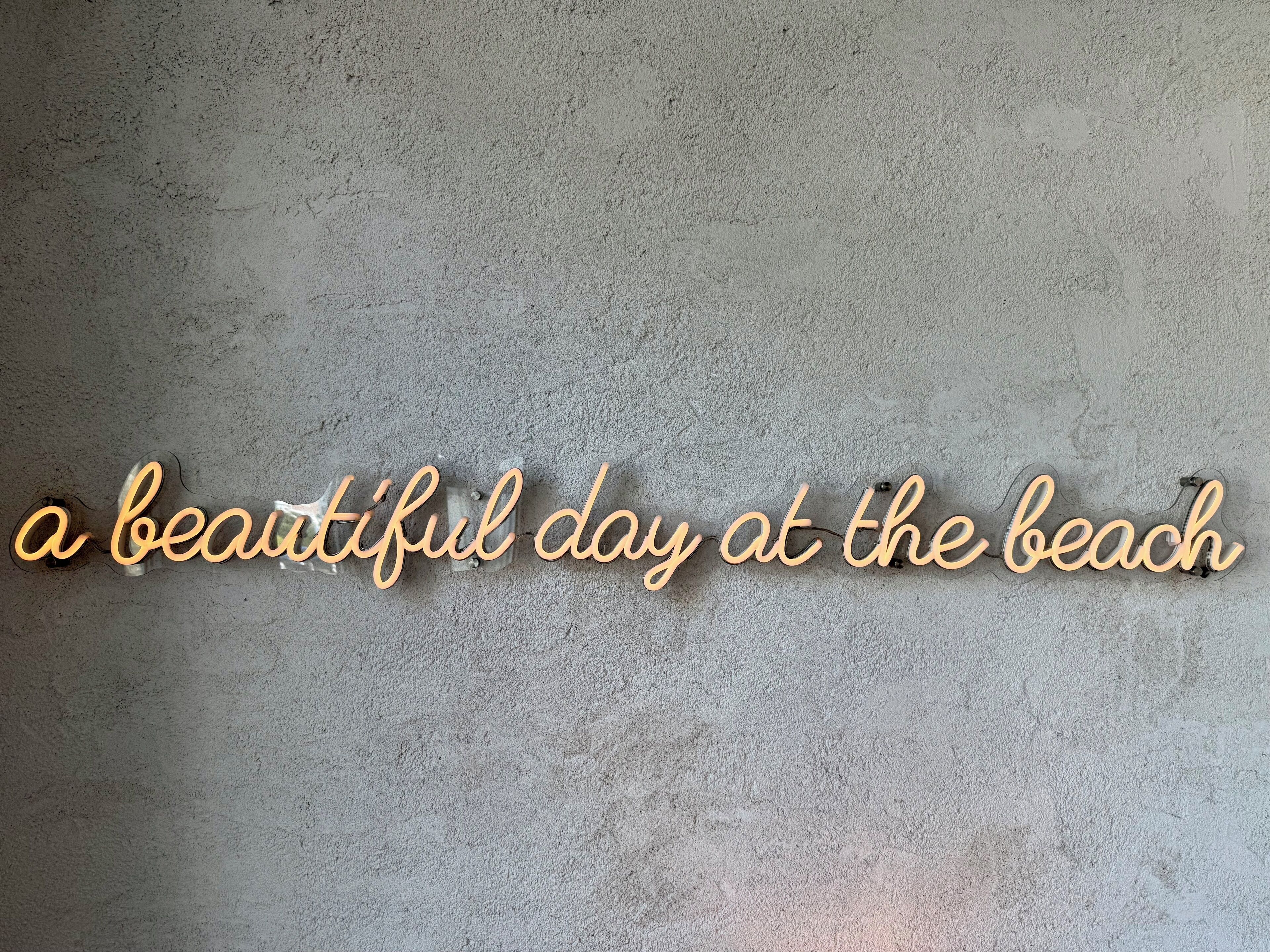 Un mur à texture avec une enseigne décorative sur laquelle on peut lire : « Une belle journée à la plage ».