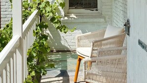 En inglasad veranda med vita tegelväggar, en glasdörr och möbler i rotting.