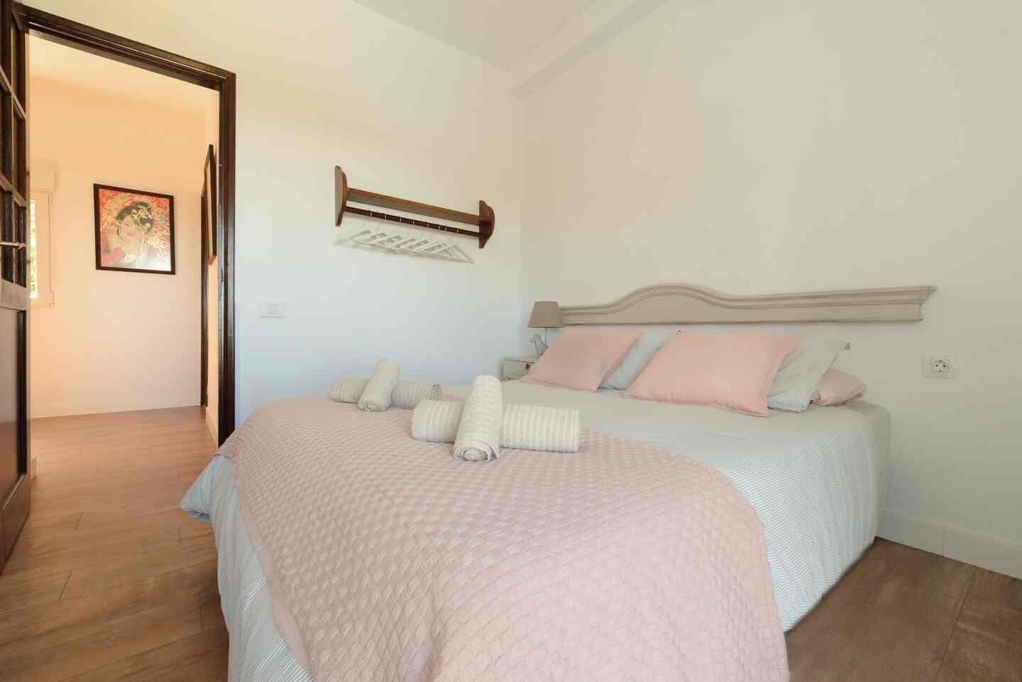 A bedroom with a bed, pillows, a headboard, a wall-mounted towel rack, and a door leading to another room.