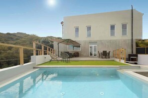 Un bâtiment moderne doté d’une piscine, d’un espace extérieur aménagé et offrant une vue sur les collines.