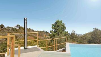 Una piscina con cubierta de madera y un poste de metal, rodeada de follaje y colinas.