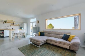 A modern living room with a sectional sofa, a dining area with a table and chairs, and a large window providing a view.