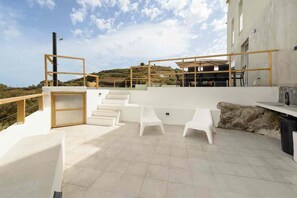 A rooftop terrace with a seating area, a staircase, and a view of the surrounding landscape.