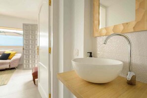 Une salle de bain moderne avec un lavabo sur colonne blanc, un plan de toilette en bois et un mur miroir.