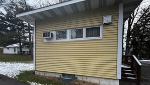 A single-story building with a flat roof, a front porch with a wooden railing, and a small window with an air conditioning unit. - Cozy 1BR hotel room, Hamilton - #343 Hiawatha (Hamilton)