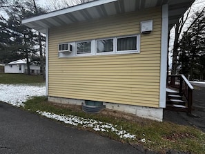 A single-story building with a flat roof, a front porch with a wooden railing, and a small window with an air conditioning unit. - Cozy 1BR hotel room, Hamilton - #343 Hiawatha (Hamilton)