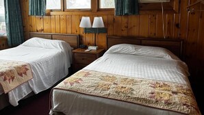 A room with two beds, wooden walls, a window, curtains, a nightstand with a lamp, and an air conditioning unit. - Cozy 1BR hotel room, Hamilton - #343 Hiawatha (Hamilton)