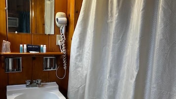 A bathroom with a wooden vanity, a white sink, a hairdryer, and a shower curtain.